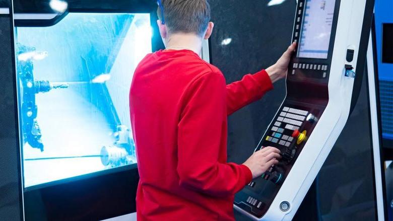 A young person watches a program run on a CNC controlled lathe.